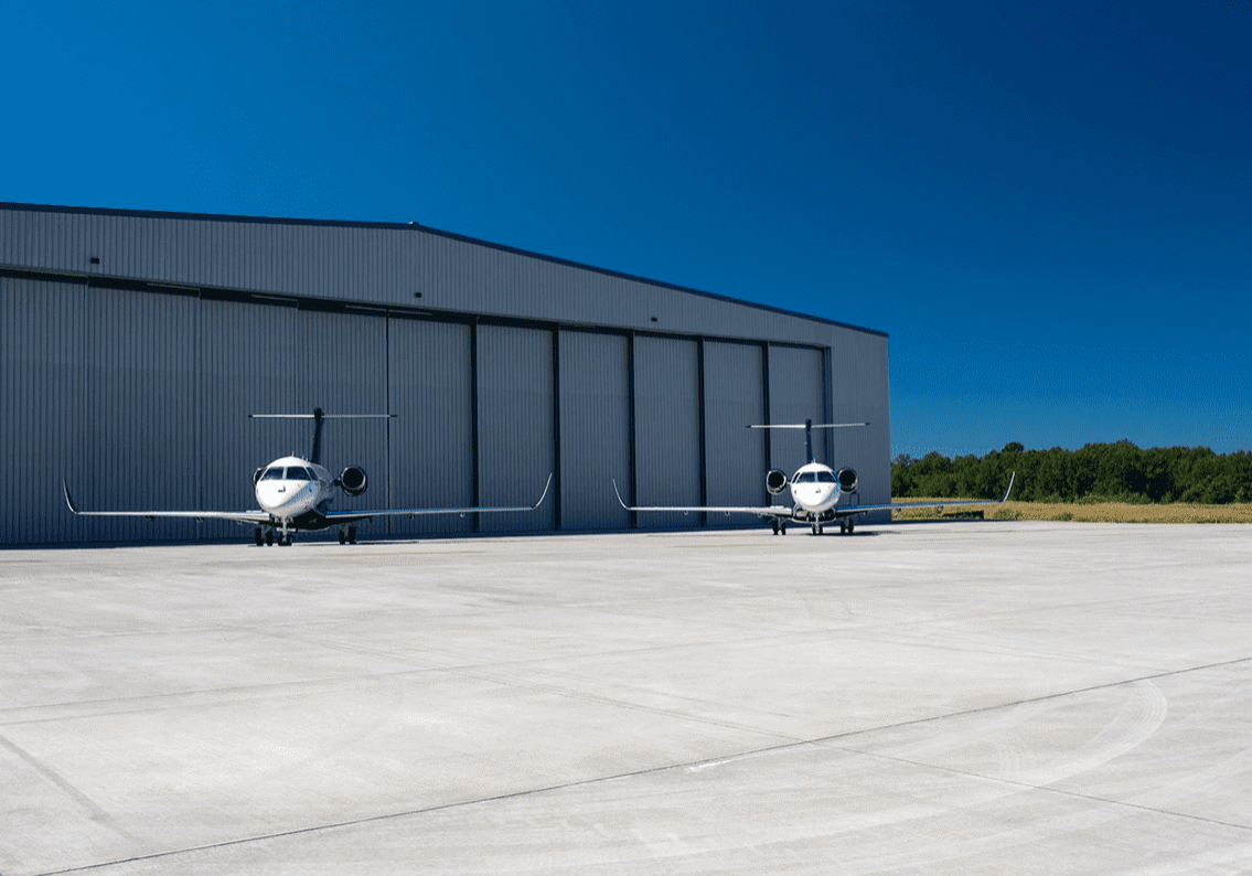 Two private jets outside large hangar.